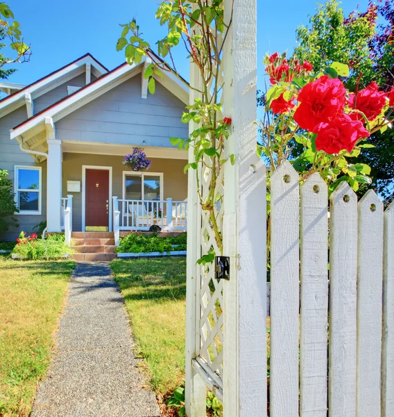 Pequeña casa y cerca blanca con rosas . — Foto de Stock