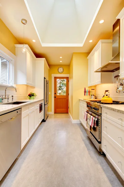 Žlutá kuchyň s bílým nábytkem a kamna. — Stock fotografie
