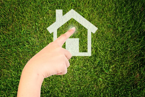 Hand pushing home icon on the grass field. — Stock Photo, Image
