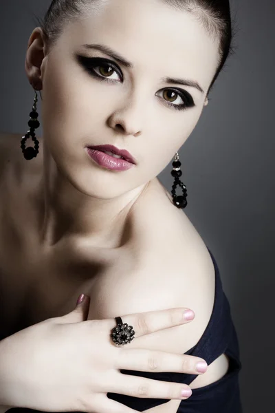 Bella ragazza con pelle perfetta in abito nero con gioielli su un retro scuro — Foto Stock