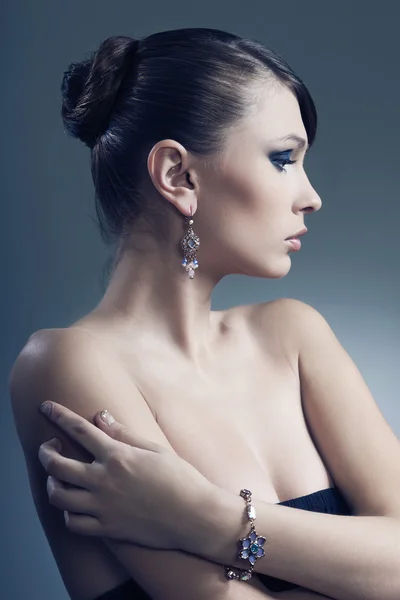 Mooie vrouw met perfecte huid in zwarte jurk met juwelen op een donkere bac — Stockfoto