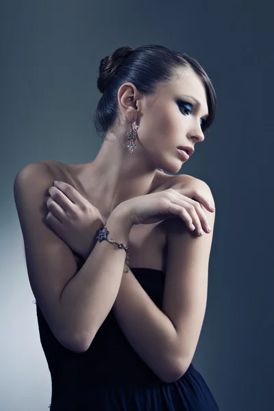 Beautiful woman with perfect skin in black dress with jewelry on a dark bac — Stock Photo, Image