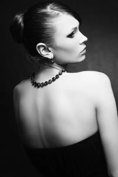 Bella donna con pelle perfetta in abito nero con gioielli su un bac scuro — Foto Stock