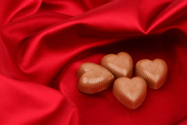 Конфеты сердца на Красная атласная — стоковое фото
