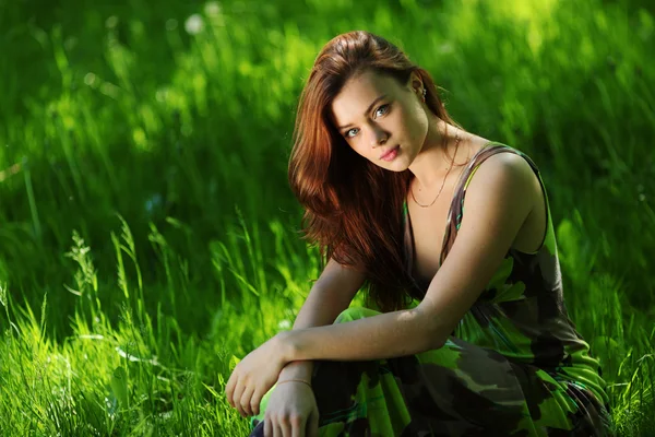 Brunette sitting on green grass — Stock Photo, Image