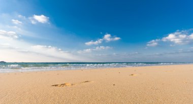 Sandy beach with lots of footprints and a blue sky with clouds clipart