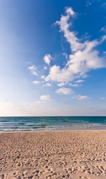 stock image Sandy beach with lots of footprints and a blue sky with clouds