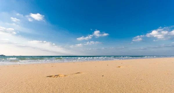 stock image Sandy beach with lots of footprints and a blue sky with clouds