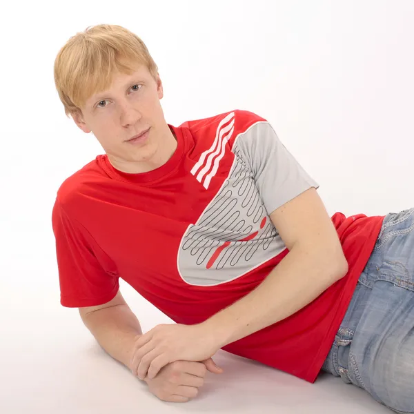 Giovane uomo in una t-shirt rossa sdraiato su uno sfondo bianco — Foto Stock