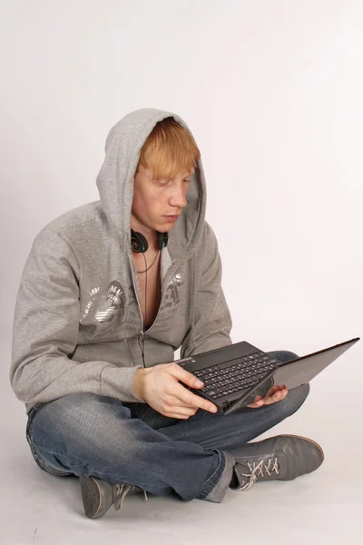 Beyaz arka plan üzerinde izole bir dizüstü bilgisayar ile katta oturan genç bir adam — Stok fotoğraf