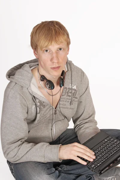 En ung man sitter på golvet med en laptop, isolerad på vit bakgrund — Stockfoto