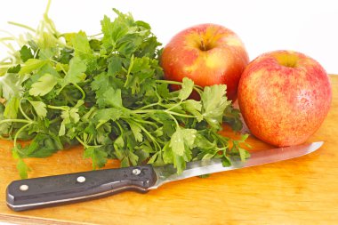 Red apples, parsley and a knife on a wooden chopping board clipart
