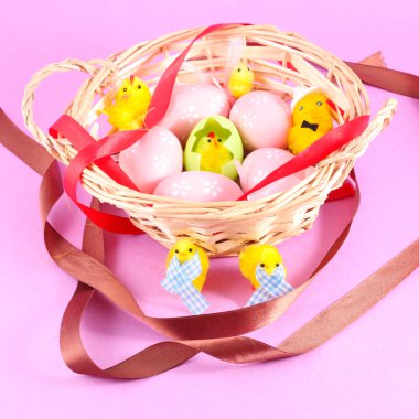 Easter basket filled with eggs and with chicken on a pink background clipart