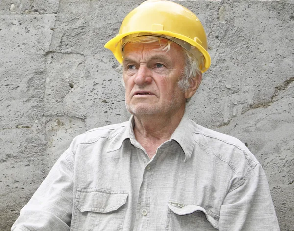 El hombre con un casco amarillo contra una pared de hormigón mira a lo lejos — Foto de Stock
