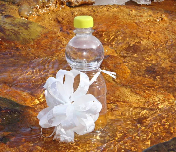 A bottle mineral waters on stones in water with a bow — Stock Photo, Image