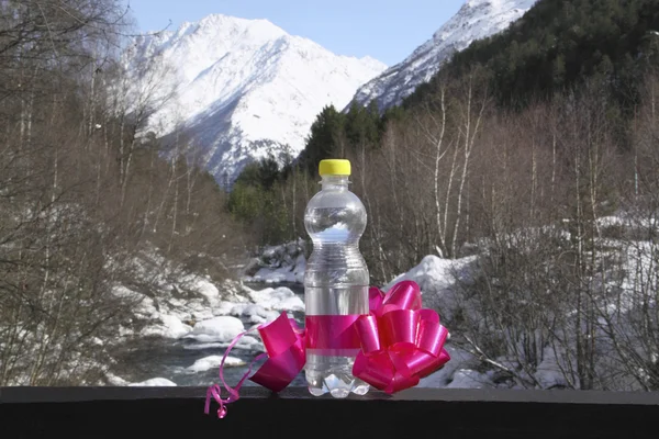 En flaska rent vatten med en båge mot snö topp — Stockfoto