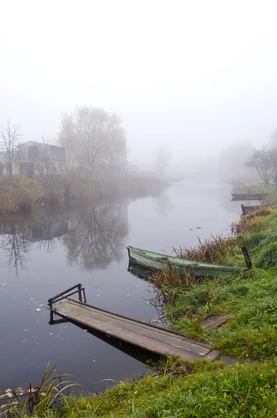 Ξύλινο καραβάκι και γέφυρα στον ποταμό βυθισμένη στην ομίχλη — Φωτογραφία Αρχείου