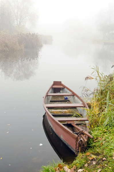Dřevěná loď na pobřeží řeky potopené v husté mlze. — Stock fotografie