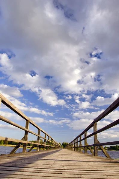Lange Holzplankenbrücke über See und bewölkten Himmel. — Stockfoto