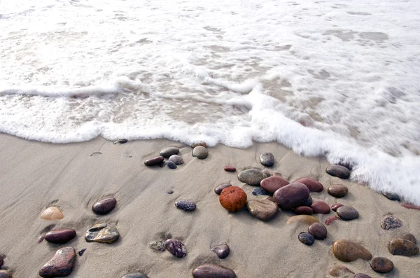 Las olas del mar golpean piedras que yacen en la arena en la costa . —  Fotos de Stock