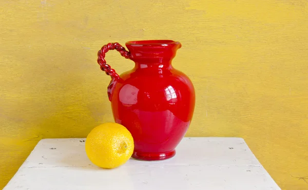 Stilleven. rode vaas en gele citroen op een plank — Stockfoto