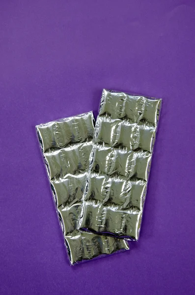 Folie verpakt chocolade stokken op violette achtergrond — Stockfoto