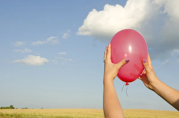 Женщина держит красный воздушный шар на фоне неба — стоковое фото
