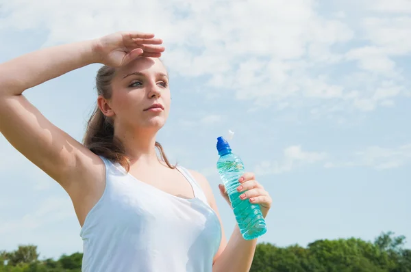 Hermosa chica bebiendo agua contra el cielo azul — Foto de Stock