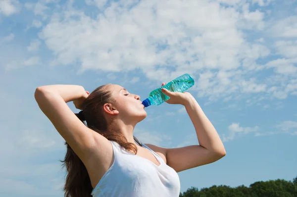Hermosa chica bebiendo agua contra el cielo azul — Foto de Stock
