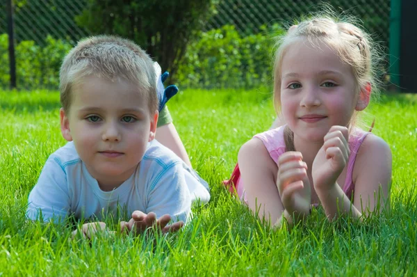 Usměvavý kluk a holčička leží na trávě v parku — Stock fotografie