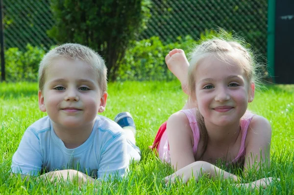 Улыбающийся мальчик и маленькая девочка лежат на траве в парке — стоковое фото