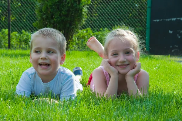 Улыбающийся мальчик и маленькая девочка лежат на траве в парке — стоковое фото