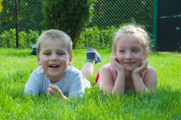 微笑的男孩和一个小女孩都躺在草地上，在公园里 — 图库照片
