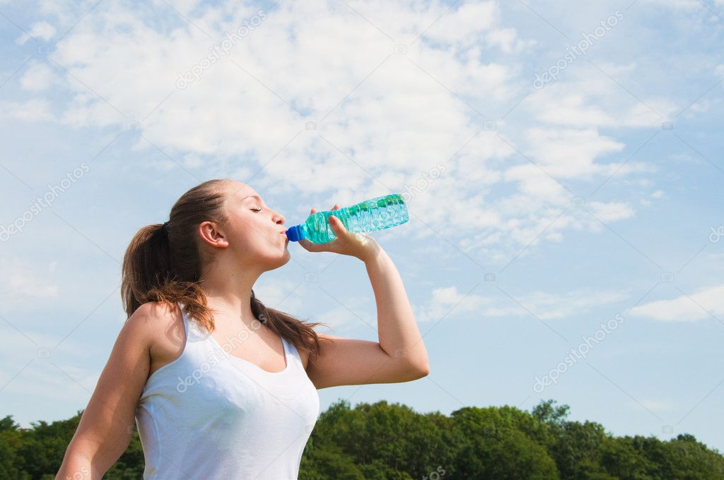Beautiful girl drinking water against blue sky