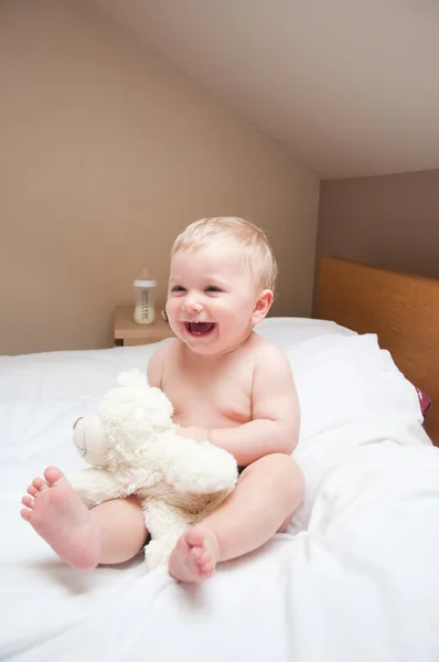 Ребенок играет в плюшевого медведя, играющего на белой кровати — стоковое фото