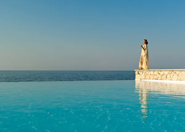Greek style woman in silk dress stand near infinity pool — Stock Photo, Image