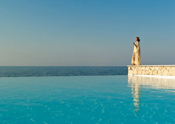 Mulher de estilo grego em vestido de seda stand perto de piscina infinito Imagens De Bancos De Imagens Sem Royalties