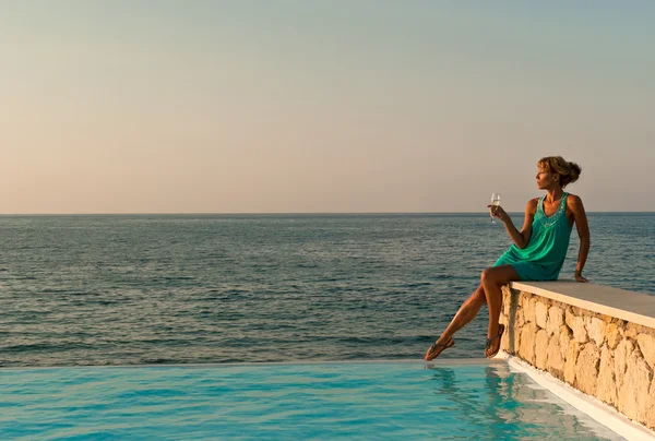 Mooie vrouw zitten op de rand van het zwembad met overstroomrand — Stockfoto