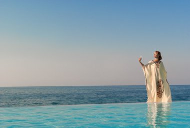 Greek style woman stand on the edge of infinity pool clipart