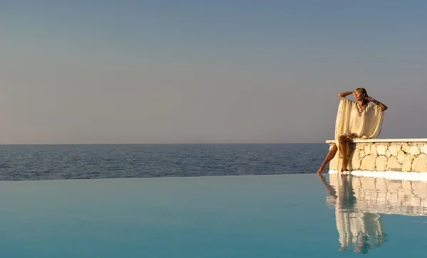 Greek style woman sitting on edge of infinity pool — Stock Photo, Image