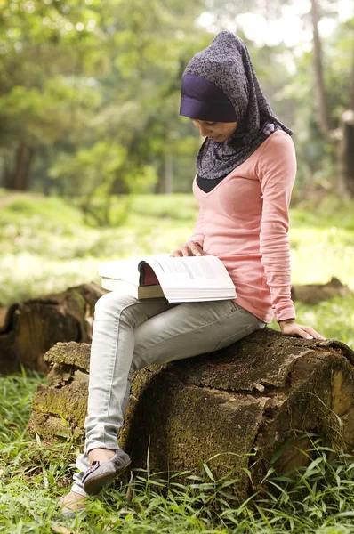 Bela jovem muçulmano senhora sentar no stump leitura — Fotografia de Stock
