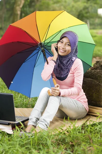 Schöne junge muslimische Dame telefoniert, während sie einen Regenschirm hält — Stockfoto