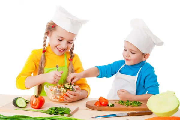 Два улыбающихся ребенка смешивают салат — стоковое фото
