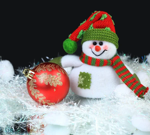 Bonhomme de neige jouet avec boule rouge festive sur un fond noir — Photo