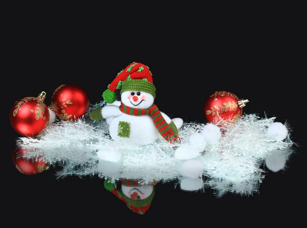 Toy snowman with a red festive ball and decorations, on a black background — Stock Photo, Image