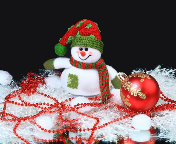 Muñeco de nieve de juguete con una bola festiva roja y decoraciones, sobre un fondo negro — Foto de Stock