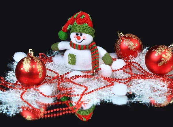 stock image Toy snowman with a red festive balls and decorations, on a black background