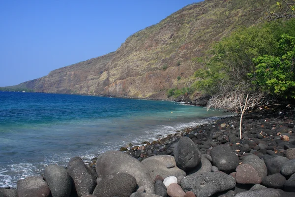 Svarta stenar på en oceanside strand med ett berg i bakgrunden — Stockfoto