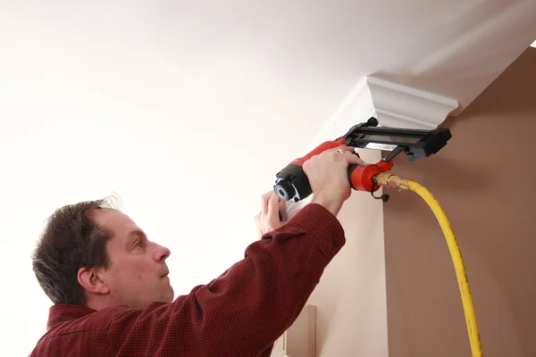 Carpintero profesional clavando corona moldeando a la pared durante la mejora del hogar Imagen de archivo