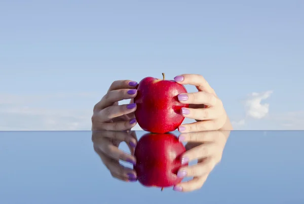 Girls hands holding apple on mirror — Stock Photo, Image
